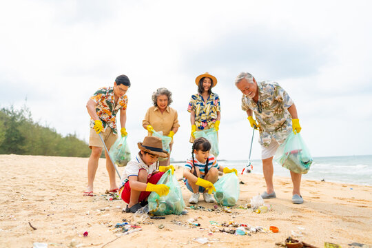 Group of Volunteers multi-Generation family picking up plastic trash and garbage together at the beach on summer holiday vacation. Environmental conservation earth day and waste pollution concept.