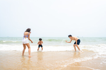 Fototapeta na wymiar Happy Asian family travel ocean on summer holiday vacation. Parents and little son in swimwear have fun outdoor activity lifestyle walking and playing sea water together at tropical beach in sunny day