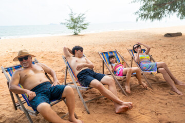 Group of Happy Multi-Generation Asian family in swimwear enjoy and fun outdoor lifestyle resting on beach chair together at tropical island beach during travel ocean on summer holiday vacation.