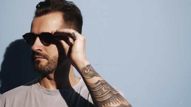 Portrait of handsome confident stylish hipster lambersexual model. Sexy man dressed in jeans jacket. Fashion male isolated on blue wall in studio. In sunglasses