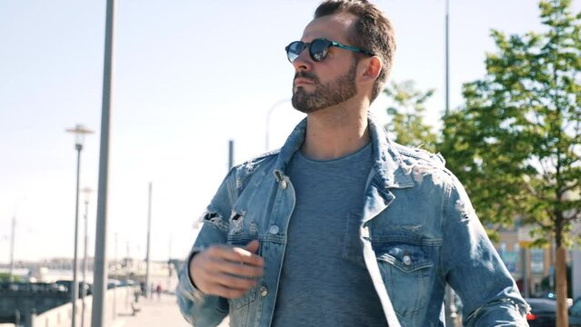 Portrait of handsome confident stylish hipster model. Sexy man dressed in jeans jacket. Fashion male posing in the street. In Europe city. Outdoors at sunny day. In sunglasses