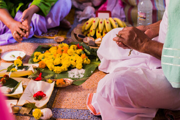 Obraz na płótnie Canvas Hindu puja rituals being performed with flowers in front of priest during pooja, wedding, funeral ceremonies. Miscellaneous religious essentials are kept in front. A person is folding hands to worship