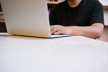 image of a young man working on his laptop in library, rear view of business man hands busy using laptop at office desk, young male student typing on computer sitting at wooden table