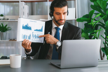 Business man wearing headphone present financial data or BI paper via laptop during online meeting....