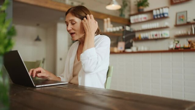 Handsome mature woman in white shirt typing on laptop in cafe