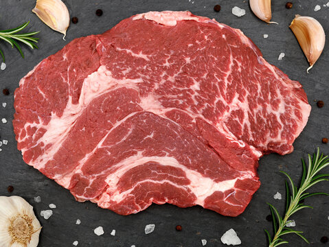 Top View Of A Raw Chuck Eye Beef Steak With Herbs, Spices And Garlic On A Slate Serving Board