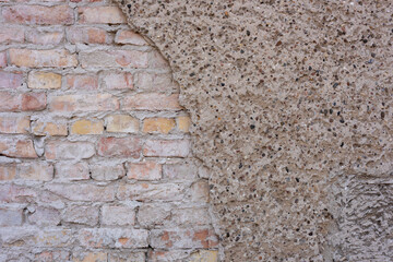 Close-up view of a partially plastered brick wall showing a transition between rough stucco and exposed aged bricks 