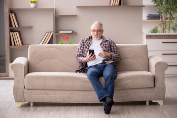 Obraz premium Old man speaking by phone at home