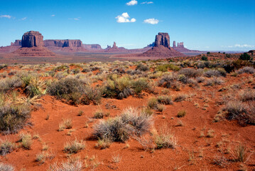 Grand landscape of Monument Valley with red sand, grass and rock formations in front of a bold blue sky - analogue photography