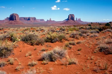 Papier Peint photo Brique Grand landscape of Monument Valley with red sand, grass and rock formations in front of a bold blue sky - analogue photography