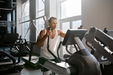 Sweaty sportsman doing cardio exercise on orbitrack training apparatus