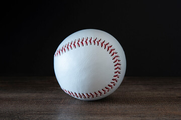 Close-up of a white baseball with red stitching on a black and wooden background