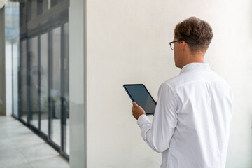 Businessman back view standing with tablet in hands, business hall