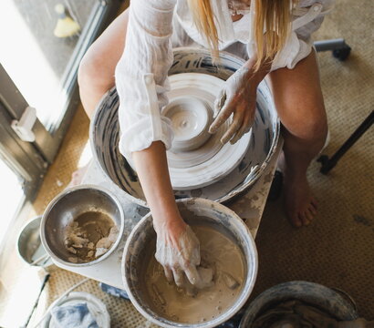 A young ceramist woman sits behind a potter's wheel,