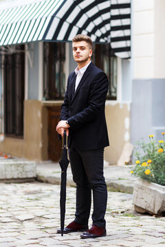 European man in a suit stands with an umbrella on the street