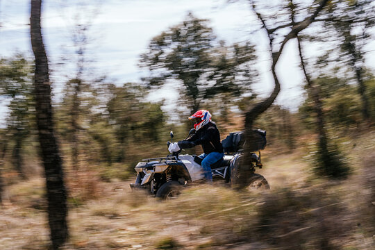Sweeping stock photo of man riding a quad bike between forest