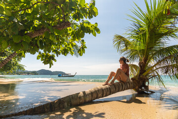 Traveler woman sitting on palm tree enjoying the beach and sea