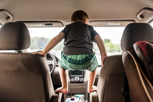 Toddler boy crouching on armrests between front seats of minivan