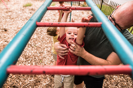 Toddler boy doing monkey bars with help from dad - Powered by Adobe