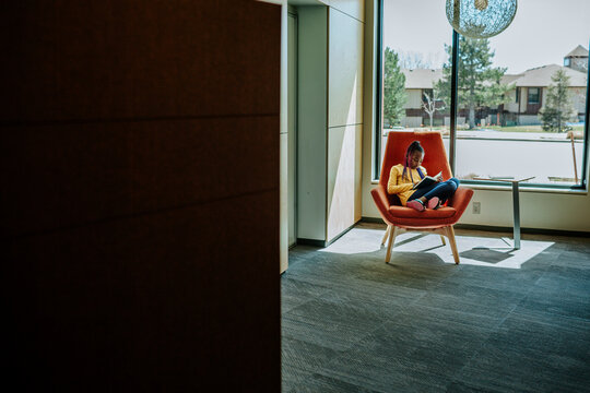 pull back of young black girl reading in front of a window