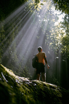 A man standing on a stone in the light looks up.