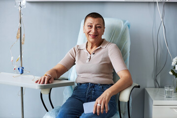 Portrait of smiling mature woman looking at camera during IV drip treatment in clinic, copy space
