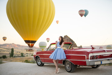beautiful girl in retro style posing near a vintage red cabriolet car on background of balloons in...