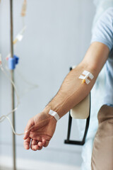 Vertical closeup of male hand with IV drip infusion in treatment session at clinic