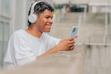 young latin male with headphones and mobile phone in the street