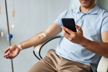 Naklejka na ściany i meble Closeup of unrecognizable man using smartphone during IV drip treatment, copy space