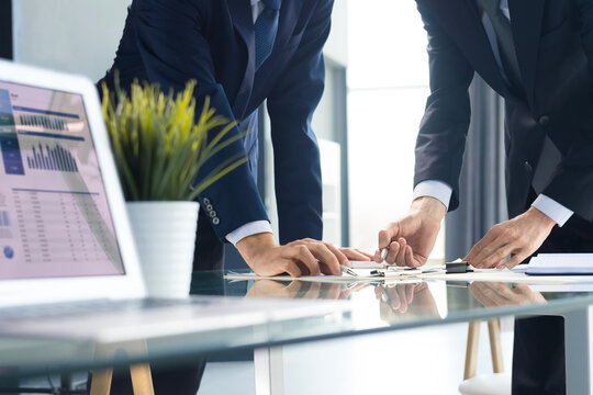 Business professionals working together at office desk, analyzing financial statistics displayed on the laptop screen.