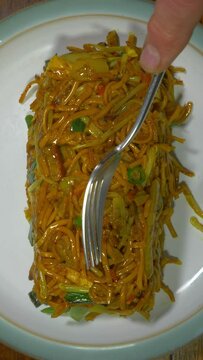 Vertical video social media format – Closeup overhead shot of a man’s hands tipping a takeout carton of hot Chinese chicken and vegetable stir fried noodles onto a plate, then spreading with a fork.