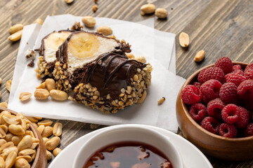 Sliced sweet cake with banana, chocolate glaze, milk filling and peanuts