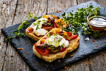 Tasty sandwiches - toasted bread with burrata cheese, anchovies, bell pepper, olives, tomatoes and...
