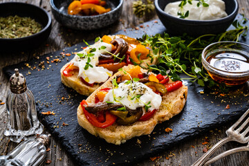 Tasty sandwiches - toasted bread with burrata cheese, anchovies, bell pepper, olives, tomatoes and...