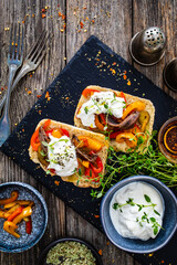 Tasty sandwiches - toasted bread with burrata cheese, anchovies, bell pepper, olives, tomatoes and thyme on wooden table
