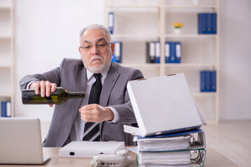 Old male employee drinking alcohol at workplace