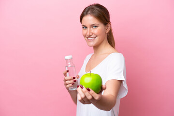 Young caucasian woman isolated on pink background with an apple and with a bottle of water