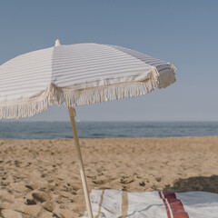 Minimal summer holidays vacation concept. Beach umbrella, beach towel on sand in front of blue sky...