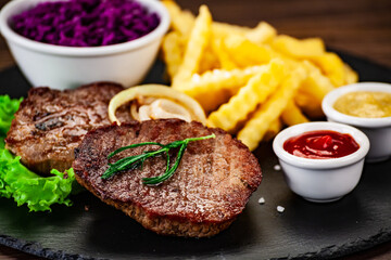 Barbecued meat, french fries, asparagus and vegetables on wooden board 