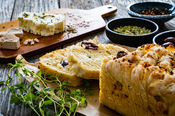 Loaf of village, fresh bread with feta and black olives on wooden table

