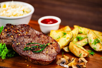 Barbecued meat, french fries and vegetables on wooden board 