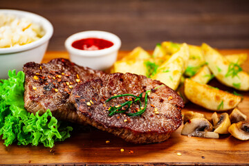 Barbecued meat, french fries and vegetables on wooden board 