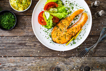 Fried salmon steak and fresh vegetable salad served on wooden table
