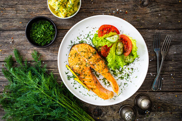 Fried salmon steak and fresh vegetable salad served on wooden table
