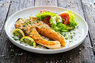 Fried salmon steak and fresh vegetable salad served on wooden table
