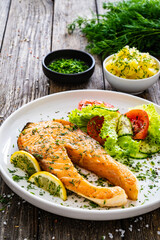 Fried salmon steak and fresh vegetable salad served on wooden table 