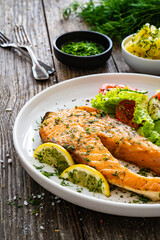 Fried salmon steak and fresh vegetable salad served on wooden table 