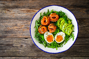 Salmon salad - smoked salmon, hard boiled eggs, avocado and leafy greens on wooden table
