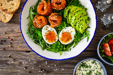 Salmon salad - smoked salmon, hard boiled eggs, avocado and leafy greens on wooden table
